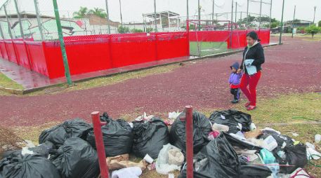 Isabel Montiel pasa con su nieto Samuel frente a varias bolsas de basura abiertas que se encuentran en una unidad deportiva de Tonalá. EL INFORMADOR / F. Atilano