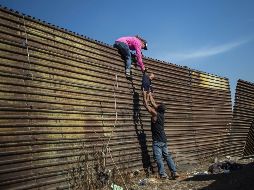 La fotografía muestra una familia de migrantes latinoamericanos que escalan una valla entre México y Estados Unidos. AFP/ Pedro Pardo