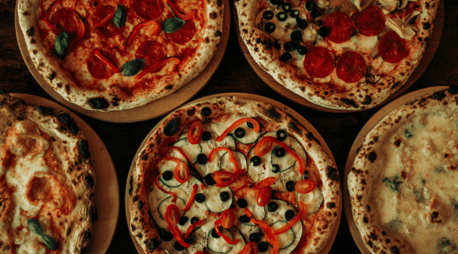 La pizza es un plato italiano, originario de Nápoles; es una base de masa de pan horneada cubierta tradicionalmente con salsa de tomate queso mozzarella y otros ingredientes. CANVA