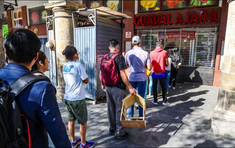 Espera frente a ventanilla. Tapatíos hacen fila en otra farmacia muy concurrida otros días, en el Centro, mientras otros observan desde la acera. EL INFORMADOR / A. Navarro