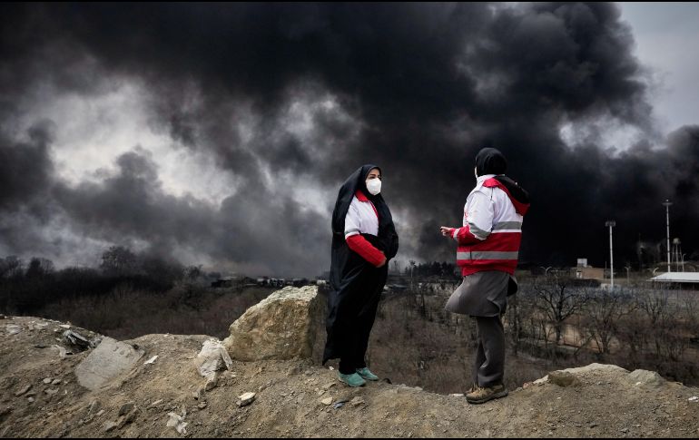 Dos mujeres de la Sociedad de la Media Luna Roja iraní permanecen de pie mientras una densa columna de humo proveniente de un ataque estadounidense-israelí contra una instalación de almacenamiento de petróleo en Teherán, Irán. AP/V. Salemi
