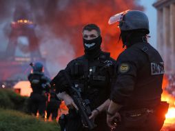 Un automóvil arde y estallan fuegos artificiales mientras la policía observa a los aficionados del PSG celebrar en París. AP/T. Padilla
