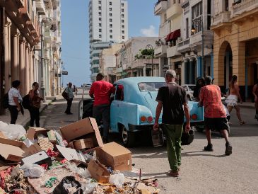 Varias personas empujan un coche clásico americano averiado junto a un montón de basura en La Habana. AP/J. Banos