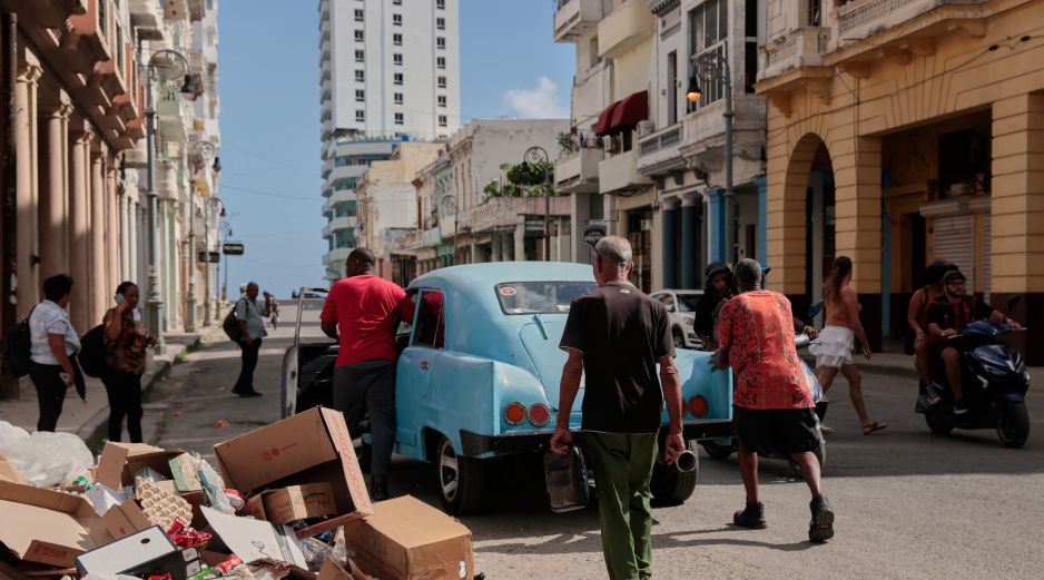 Varias personas empujan un coche clásico americano averiado junto a un montón de basura en La Habana. AP/J. Banos