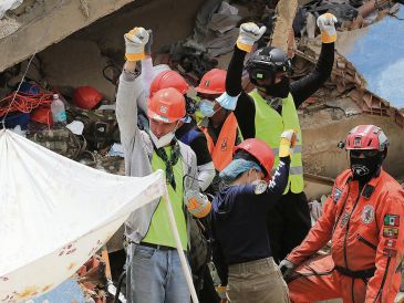 Rescatistas, entre ellos los Topos Azteca, piden silencio a los presentes tras haber escuchado sonidos bajo los escombros de un edificio. EFE